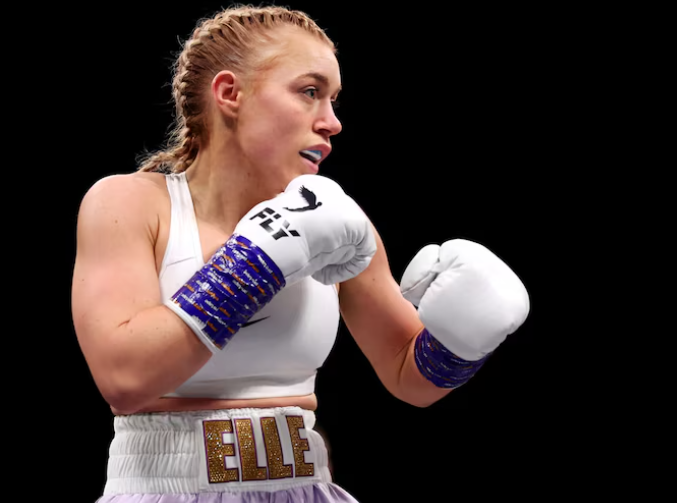 Elle Brooke in white boxing gear with 'ELLE' on her waistband, posing in fighting stance—capturing her shift from 'elle brooke porn' fame to legitimate boxing contender.
