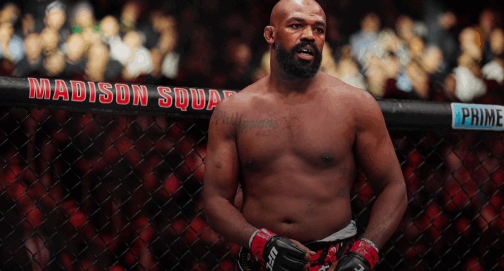 Jon Jones stands shirtless inside the UFC octagon at Madison Square Garden, wearing red gloves and focused expression, marking his return after clearing legal charges.
