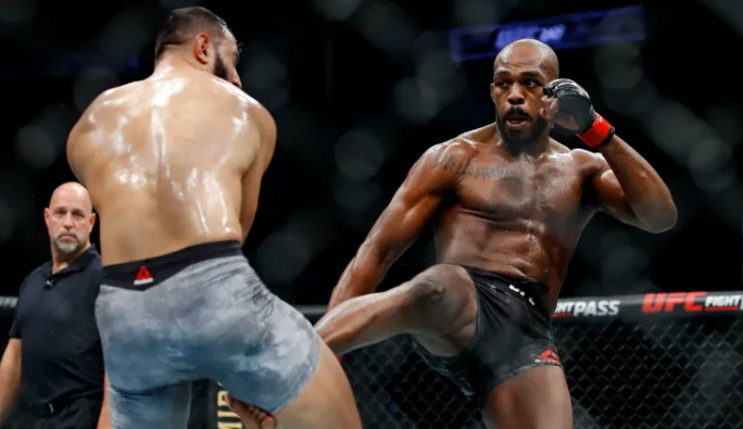 Jon Jones throws a right leg kick during a UFC fight, eyes locked on his opponent, showcasing his elite MMA striking technique inside the octagon.
