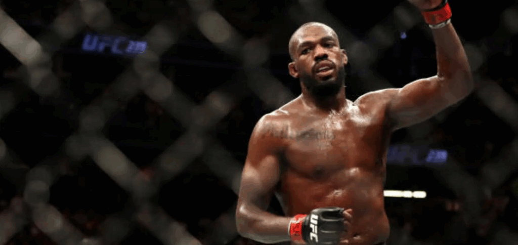 Jon Jones stands shirtless inside the UFC octagon, raising his fist in victory. The text describes allegations of leaving the scene of an accident, later challenged by Jones and his attorney Christopher Dodd.
