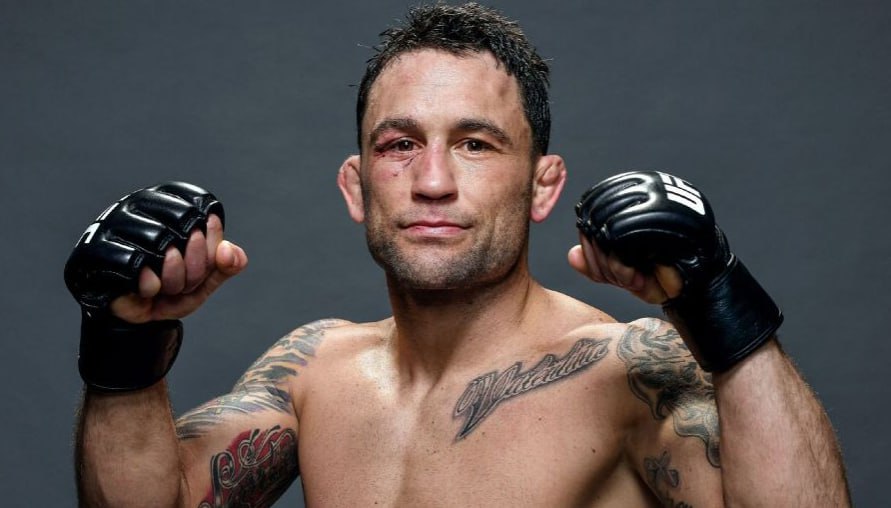MMA fighter posing with raised fists, wearing UFC gloves and showing facial bruises after a fight.
